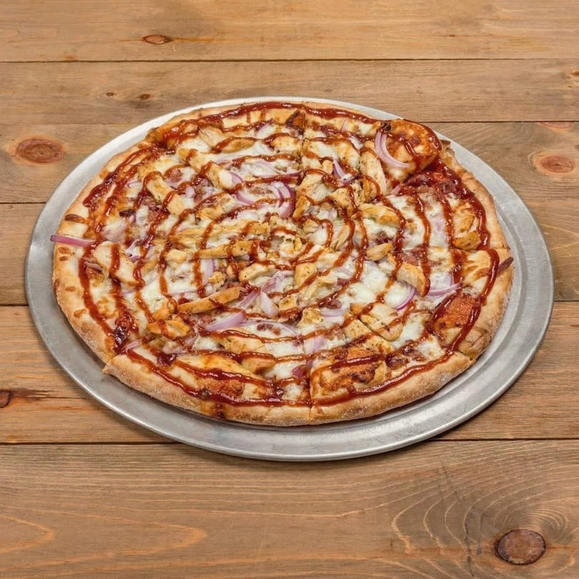 BBQ chicken pizza with red onions and a swirl of BBQ sauce on a wooden table.
