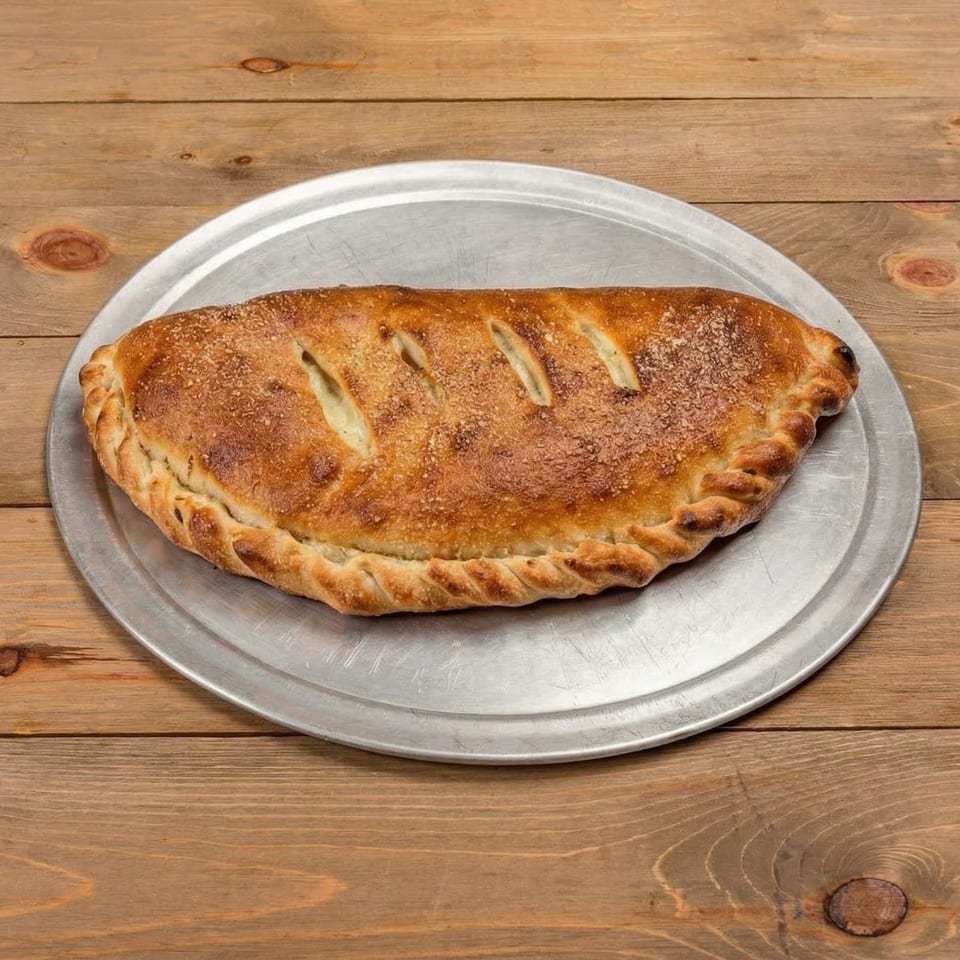 A golden-brown calzone, sprinkled with parmesan, rests on a metal pizza pan on a wooden table.