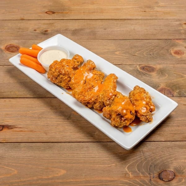 Crispy chicken wings drizzled with buffalo sauce, served with carrots and ranch dressing on a white plate.