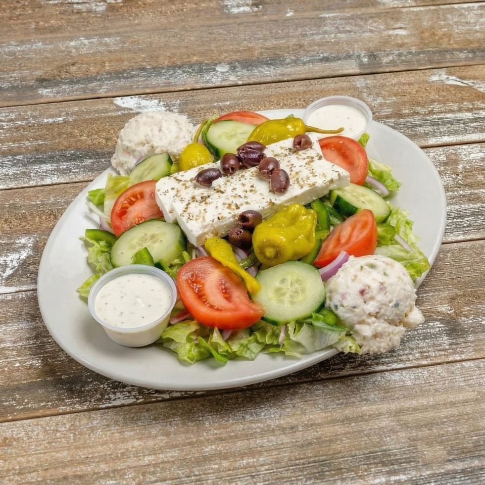 A large Greek salad with feta, olives, tomatoes, cucumbers, and pepperoncini on a white plate.