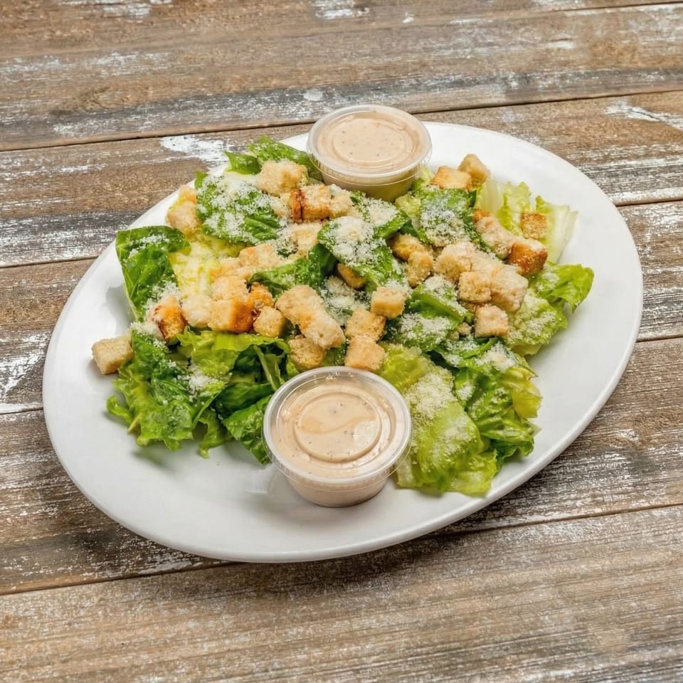 Caesar salad with croutons, parmesan cheese, and two dressing cups on a white plate.