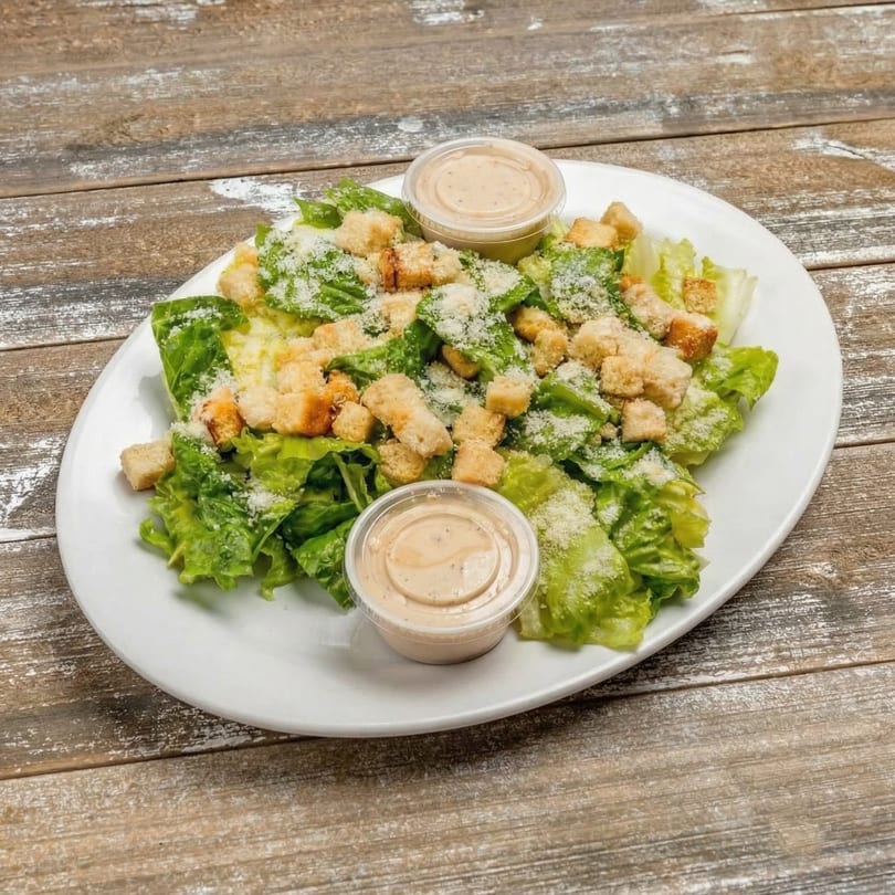 Caesar salad with croutons, parmesan cheese, and two dressing cups on a white plate.